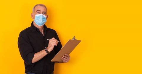 Medewerker met mondkapje heeft een pen met schrijfblok in de hand